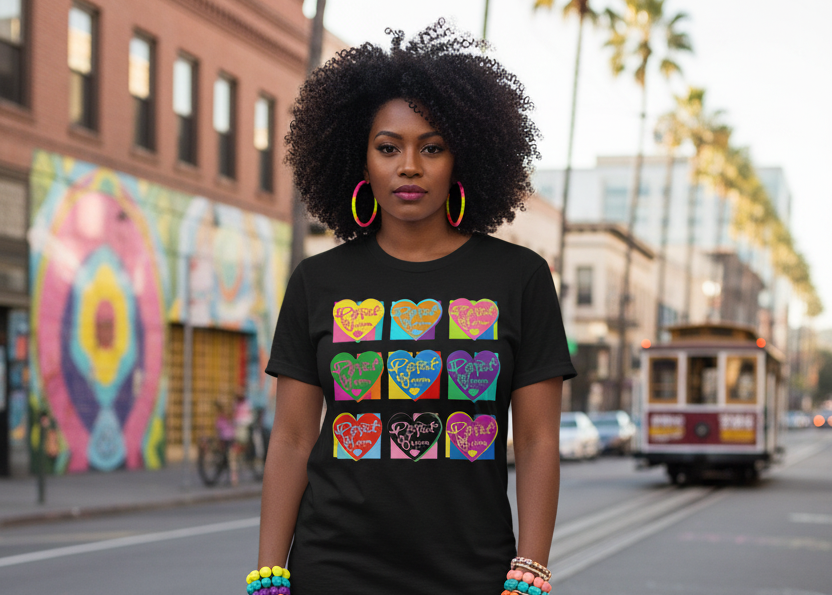 A woman stands on a city street wearing a black graphic T-shirt with a colorful grid of cartoon faces, black pants, and multicolored sneakers. The background shows a blurred urban street scene with buildings, palm trees, and a cable car.