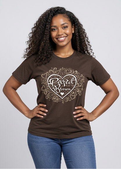 A smiling woman with curly hair wearing a brown short-sleeve t-shirt with a white graphic that reads 'Perfect Brown' inside a heart design, paired with blue jeans, against a light gray studio background.