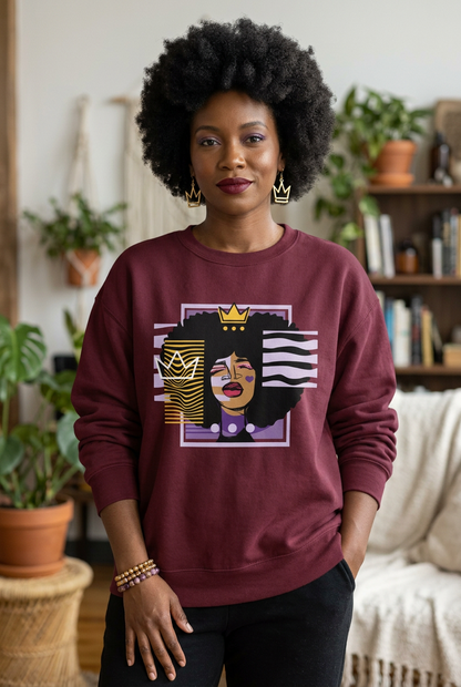A woman with an afro hairstyle wearing a maroon crewneck sweatshirt with a graphic print of a woman with an afro and a gold crown, standing in a cozy, plant-filled room.