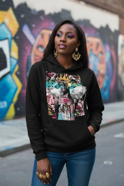 A woman wearing a black pullover hoodie with a colorful graphic print on the front, paired with blue jeans and gold jewelry, standing in front of a graffiti-covered wall.